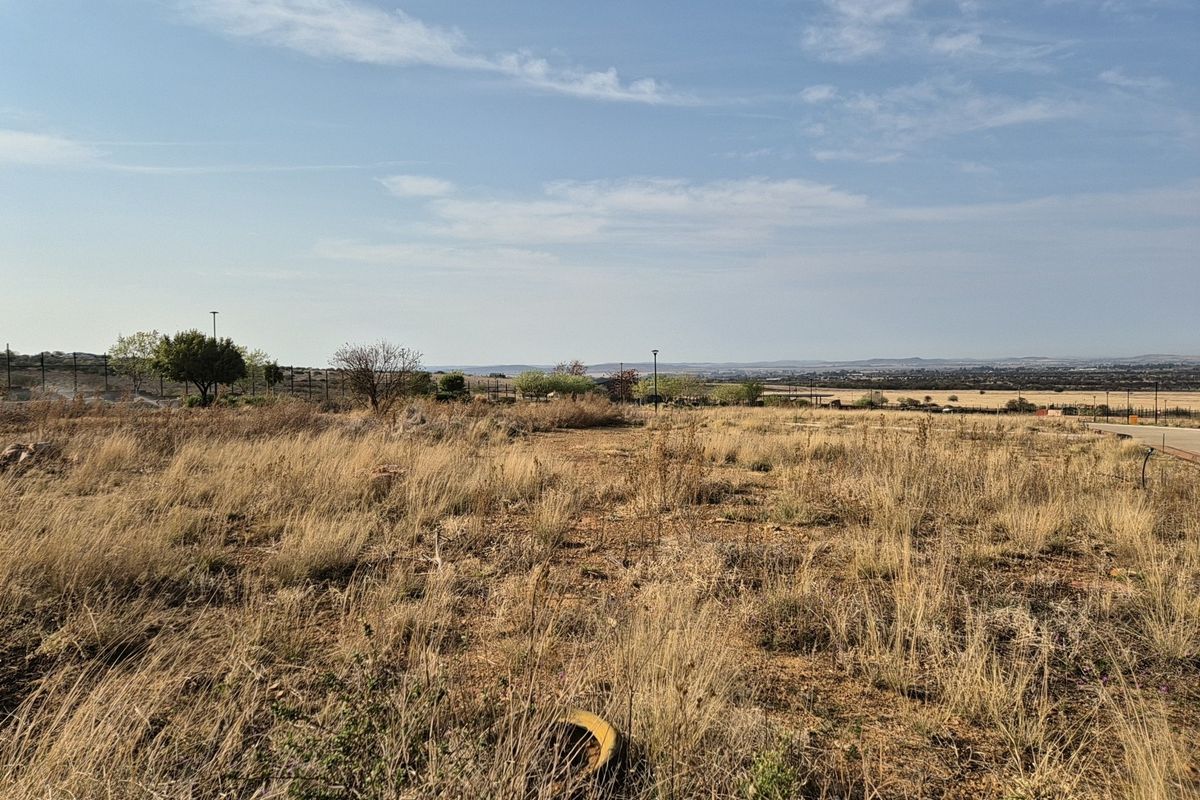 A wide-angle view of a vacant residential plot featuring dry natural vegetation, perimeter fencing, and distant landscape views.