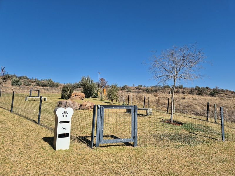 A well-maintained residential garden area featuring wire mesh fencing, a secure metal gate, and a dedicated pet waste station.