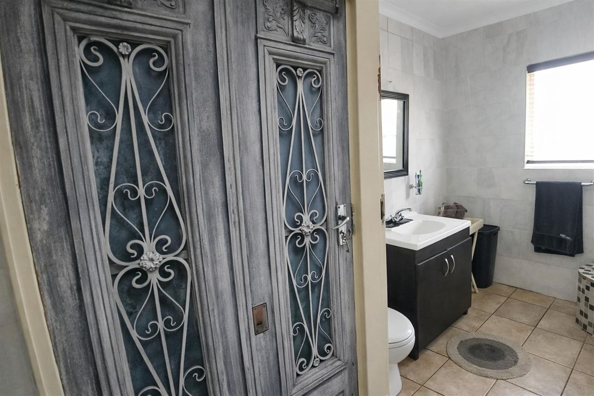 A functional bathroom featuring a vanity cabinet, basin, toilet, and tiled finishes, accessed through a decorative metal-screened door.