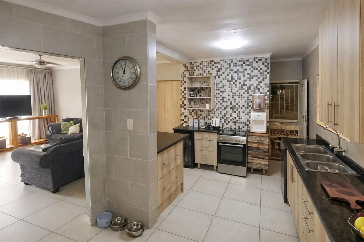A functional kitchen featuring tiled flooring, granite countertops, built-in cabinetry, and a mosaic tiled splashback, with an open-plan flow to the adjacent living area.