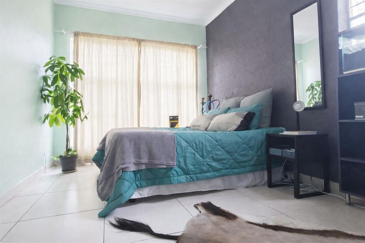A well-lit bedroom featuring neutral tiled flooring, a coved ceiling, and a contrasting dark accent wall.