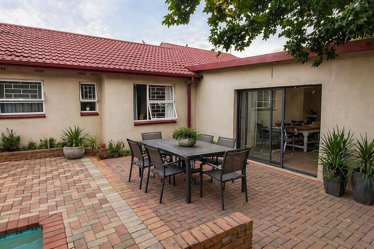 Rear exterior view featuring a brick-paved patio area, sliding glass doors leading to the interior, and a swimming pool.