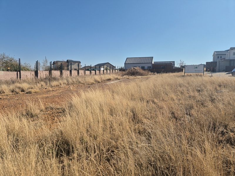 A vacant residential plot featuring perimeter walling with electric fencing and existing real estate signage in a developed estate setting.