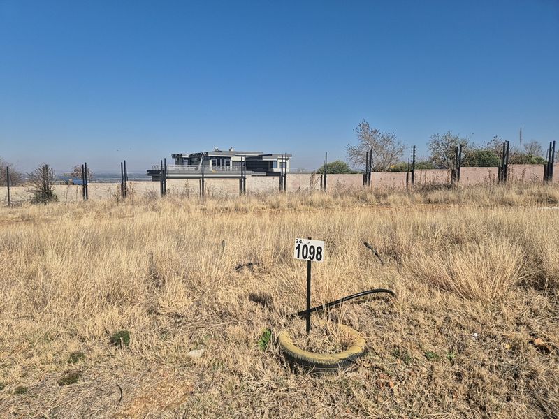 A vacant residential plot featuring dry grass, a boundary wall with electric fencing, and a clearly marked plot number.