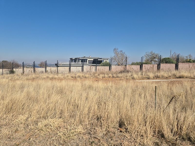 A vacant residential plot featuring dry grass, enclosed by a perimeter boundary wall and electric fencing.