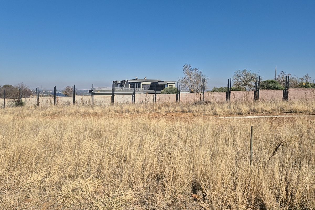 A vacant residential plot featuring dry grass, enclosed by a perimeter boundary wall and electric fencing.