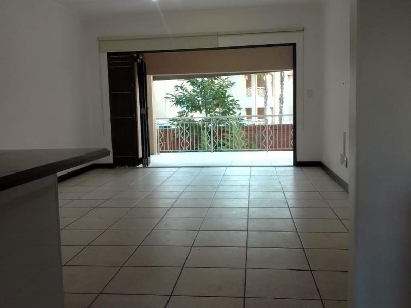 An empty open-plan living area featuring tiled flooring and a large sliding door leading out to a private balcony.