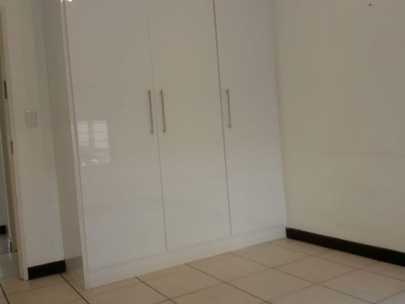 A clean, empty bedroom featuring white built-in wardrobes and neutral tiled flooring, providing a blank canvas for personalization.