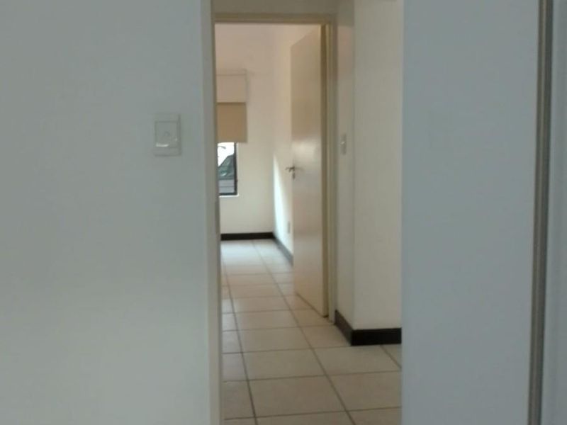 A view through a hallway with tiled flooring, connecting to an adjacent room with a window.