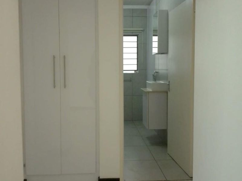 A clean hallway featuring white built-in cupboards and tiled flooring, providing direct access to an adjacent bathroom.