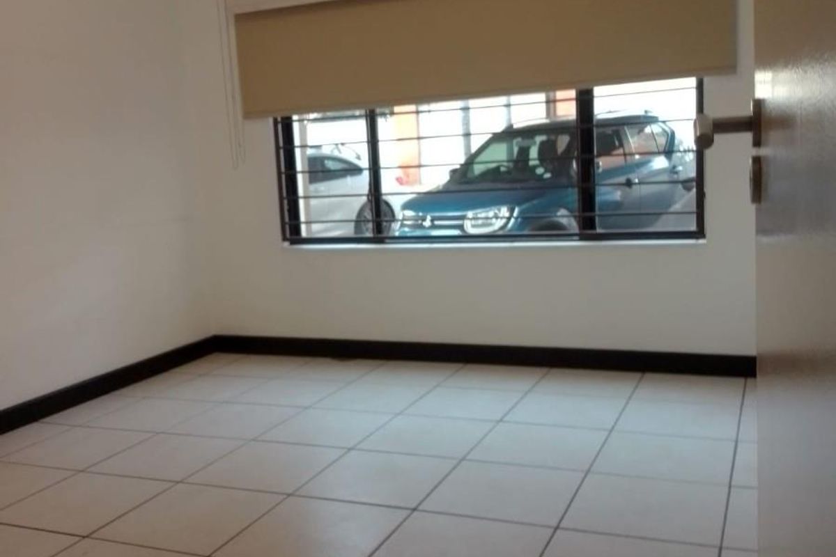 An empty bedroom featuring neutral tiled flooring, security bars on the window, and fitted roller blinds.