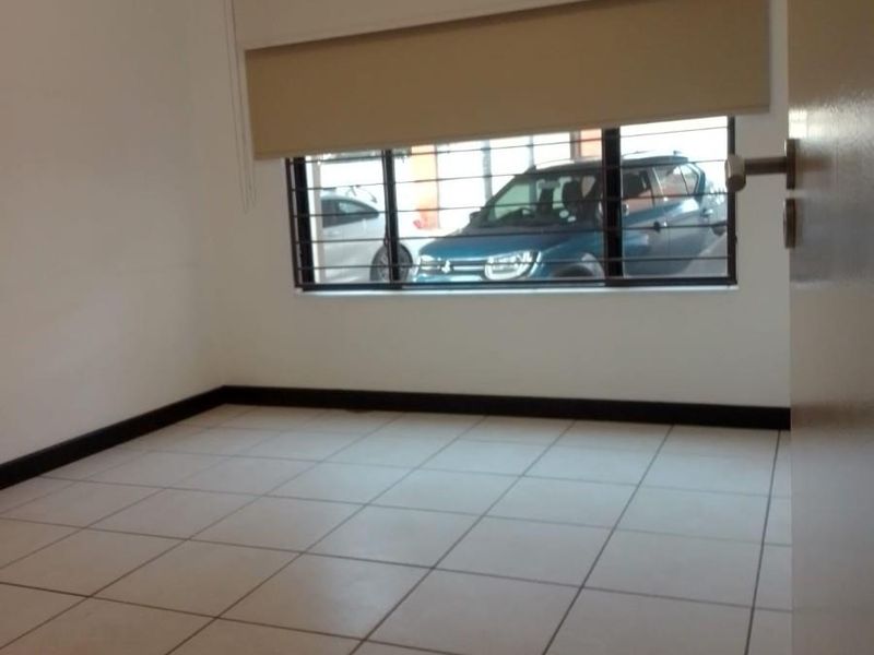 An empty bedroom featuring neutral tiled flooring, security bars on the window, and fitted roller blinds.