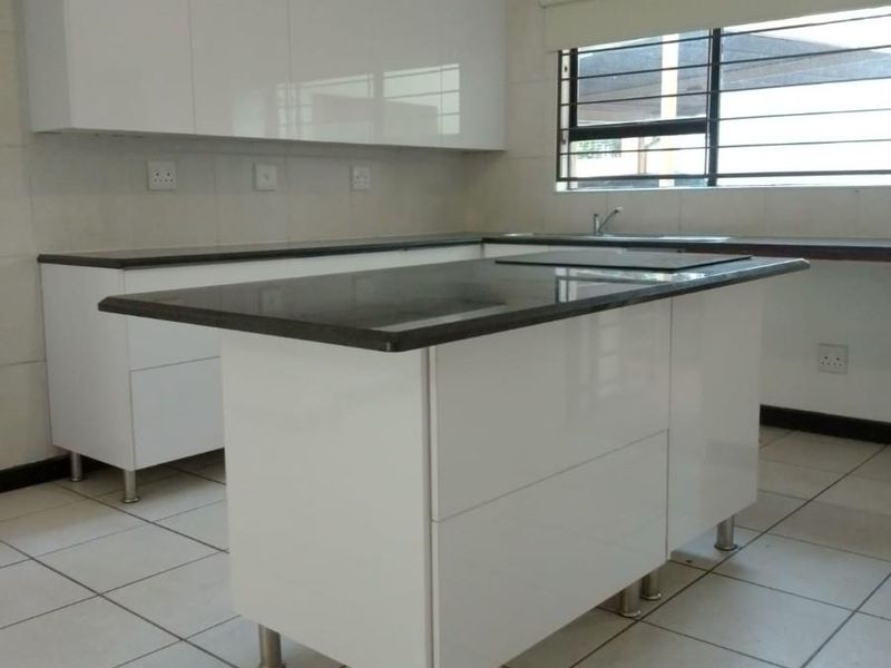 Modern kitchen featuring white gloss cabinetry, dark granite countertops, a central island, and ceramic floor tiles in a clean, well-maintained space.