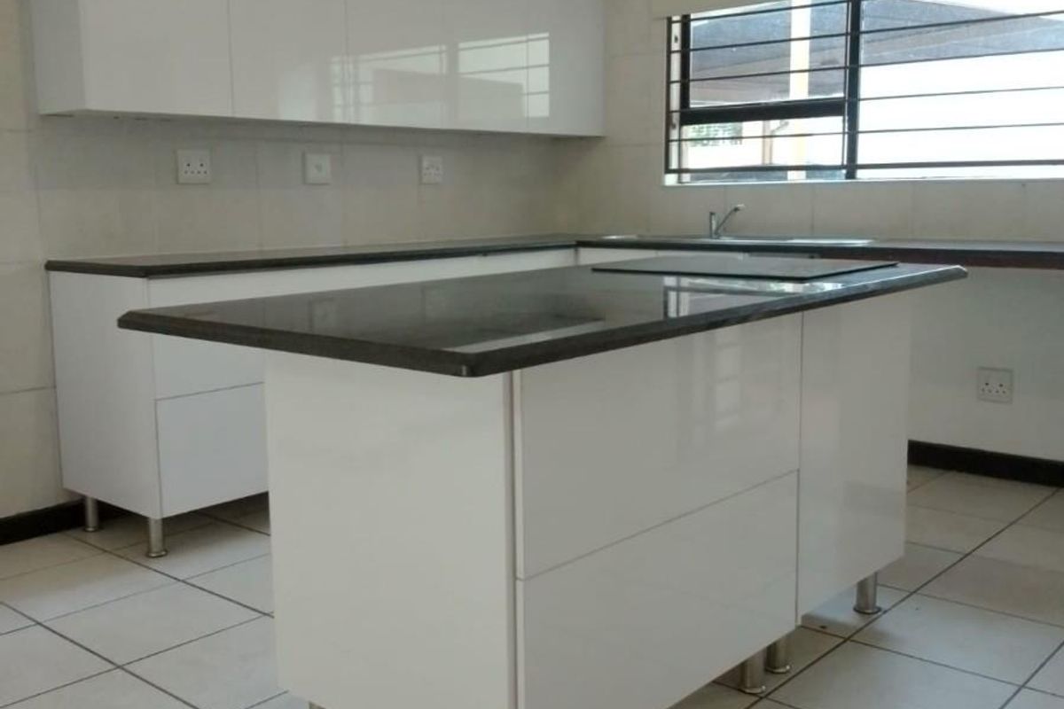 Modern kitchen featuring white gloss cabinetry, dark granite countertops, a central island, and ceramic floor tiles in a clean, well-maintained space.