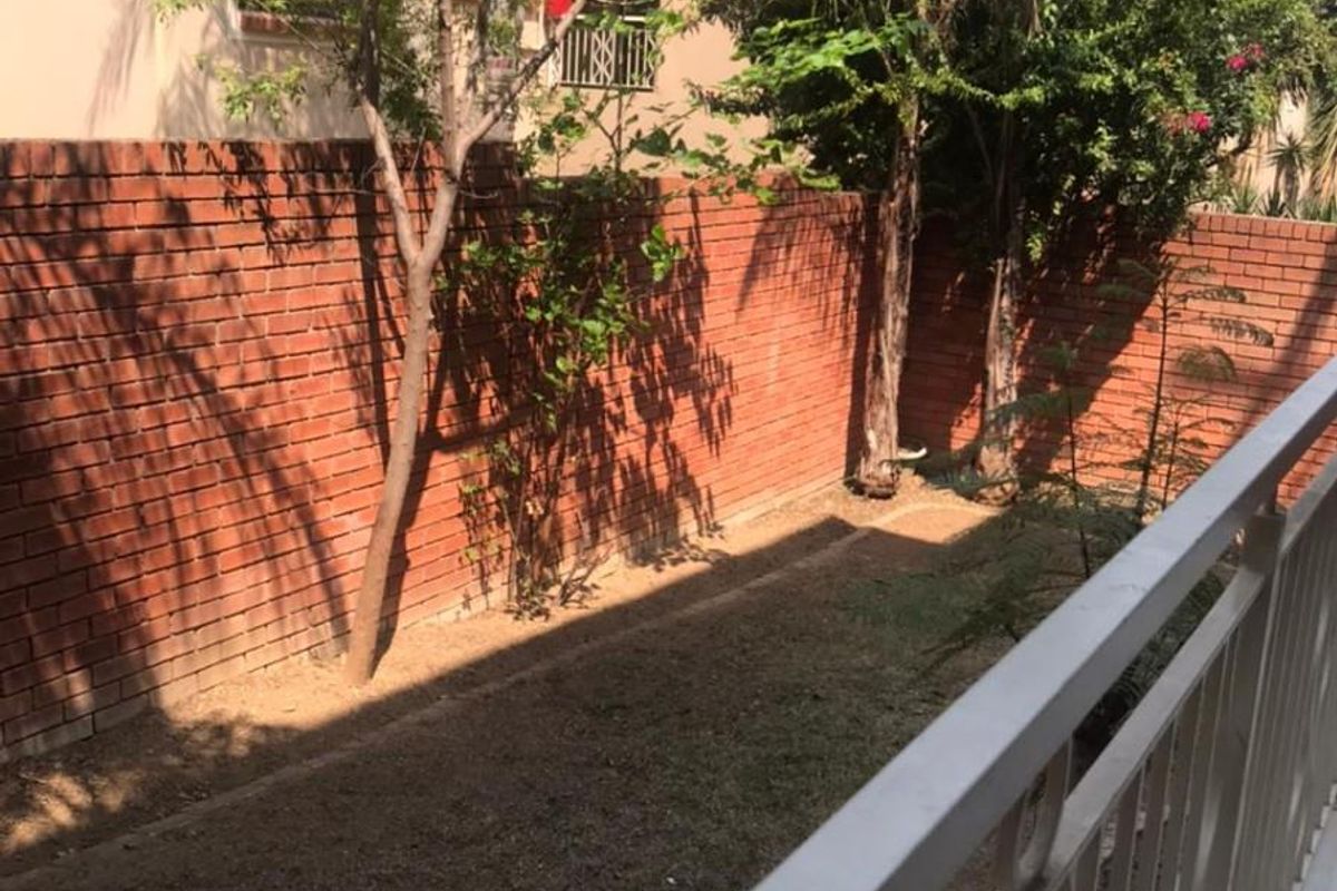 A view of a rear garden area featuring a brick boundary wall and a metal balustrade overlooking the outdoor space.
