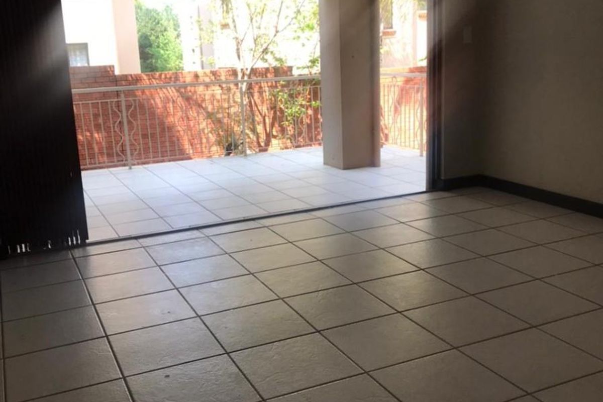 An empty living room featuring neutral tiled flooring and a large sliding glass door that opens onto a private balcony.
