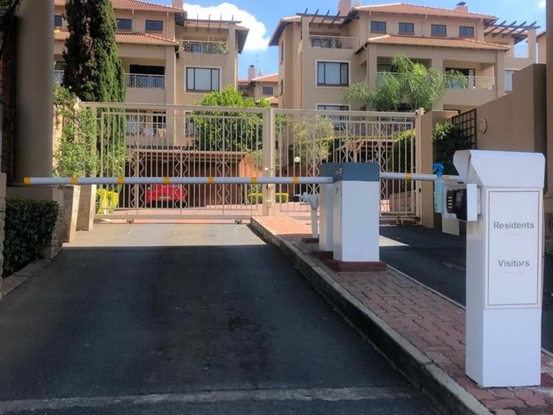 Secure gated entrance to a multi-story apartment complex featuring automated boom gates and access control systems for residents and visitors.