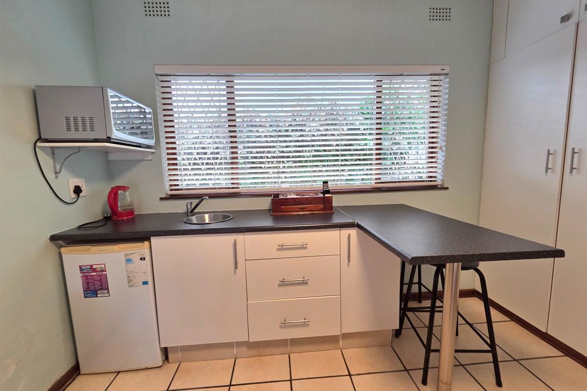 A compact kitchen area featuring white cabinetry, dark laminate countertops, a stainless steel sink, and tiled flooring with a breakfast bar extension.