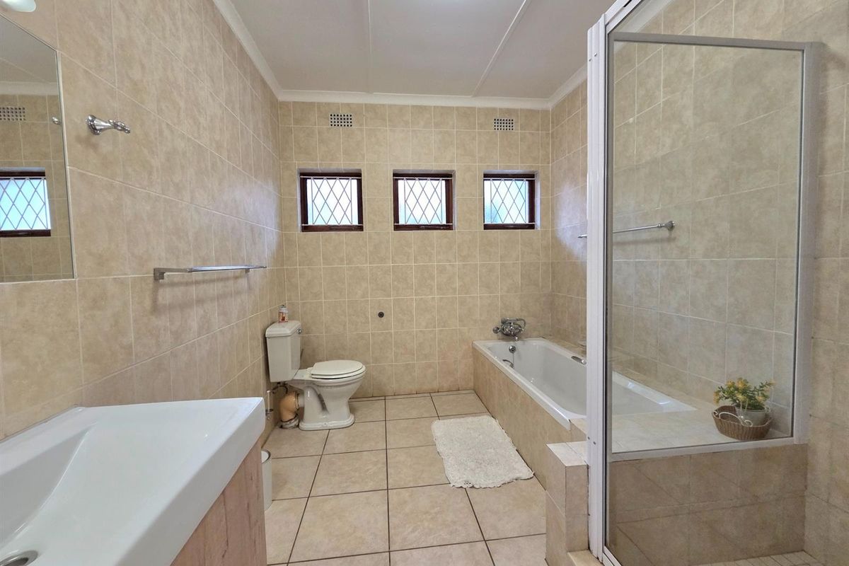 A functional bathroom featuring neutral ceramic tiling, a built-in vanity, a separate bathtub, and a glass-enclosed shower area.