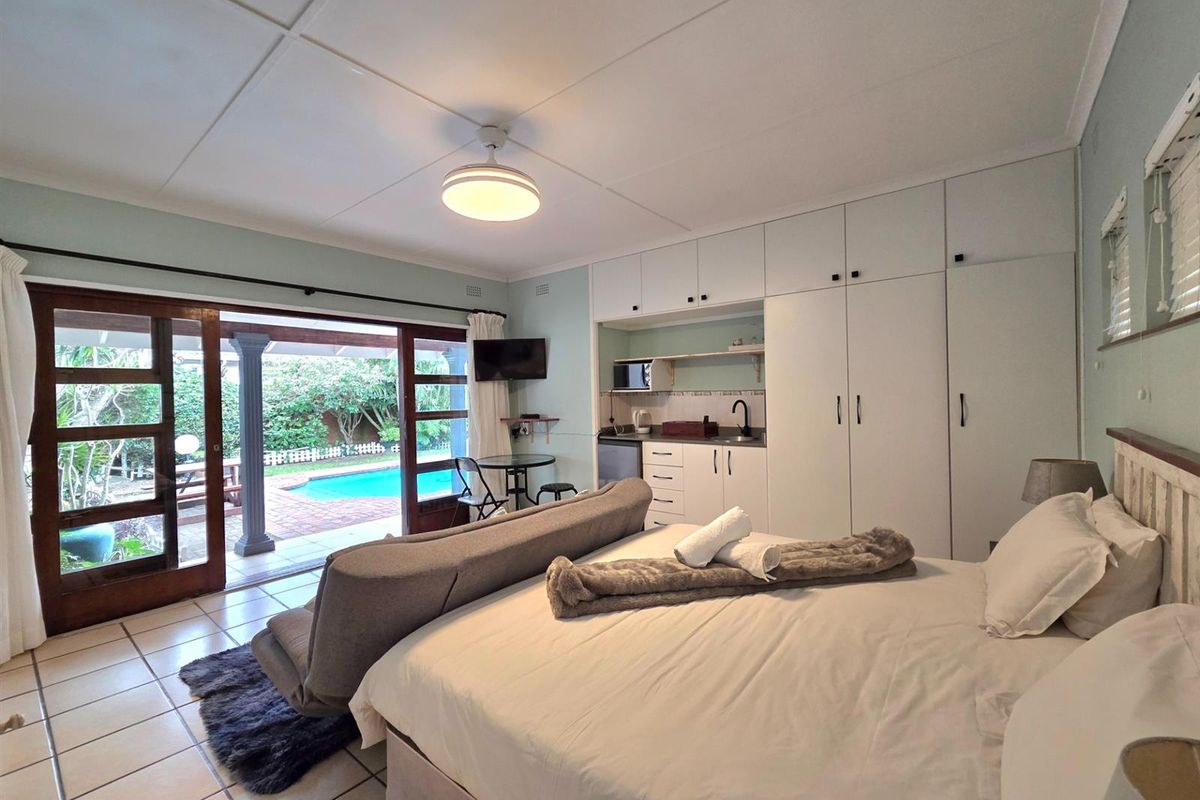 Spacious bedroom featuring built-in cupboards, a convenient kitchenette, and sliding glass doors providing direct access to the patio and pool area.