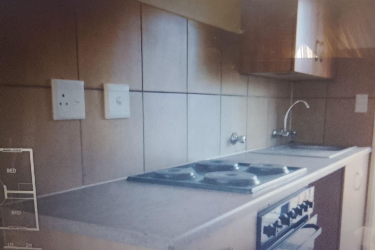 A compact kitchen featuring built-in cabinetry, a hob, an oven, and a sink with a tiled splashback.