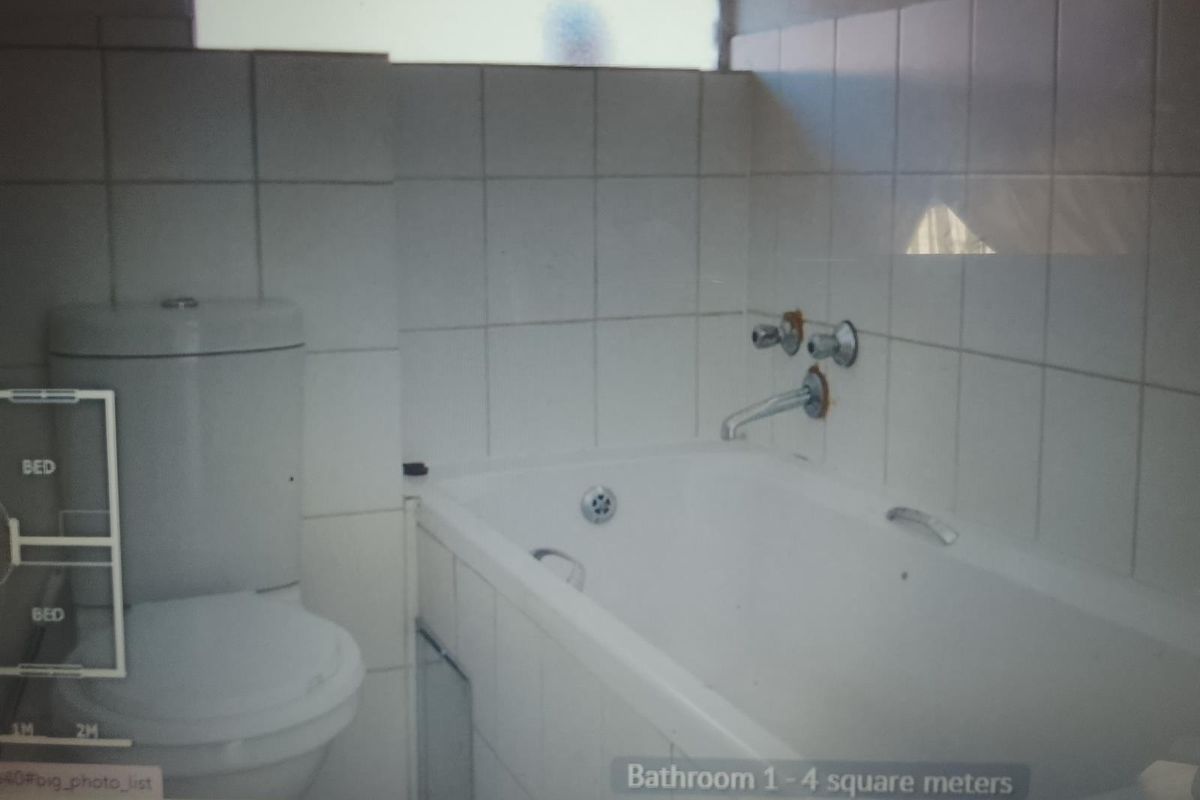 A compact bathroom featuring a standard bathtub and toilet with white wall tiling, requiring cosmetic updates to improve its dated appearance.