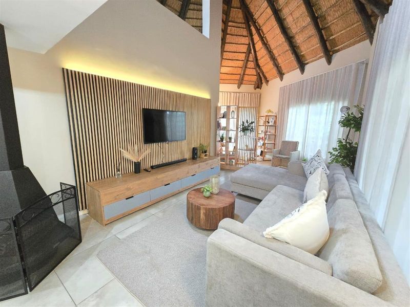 Spacious living room featuring a high vaulted thatched ceiling, modern timber slat feature wall with integrated lighting, and large windows providing natural light.