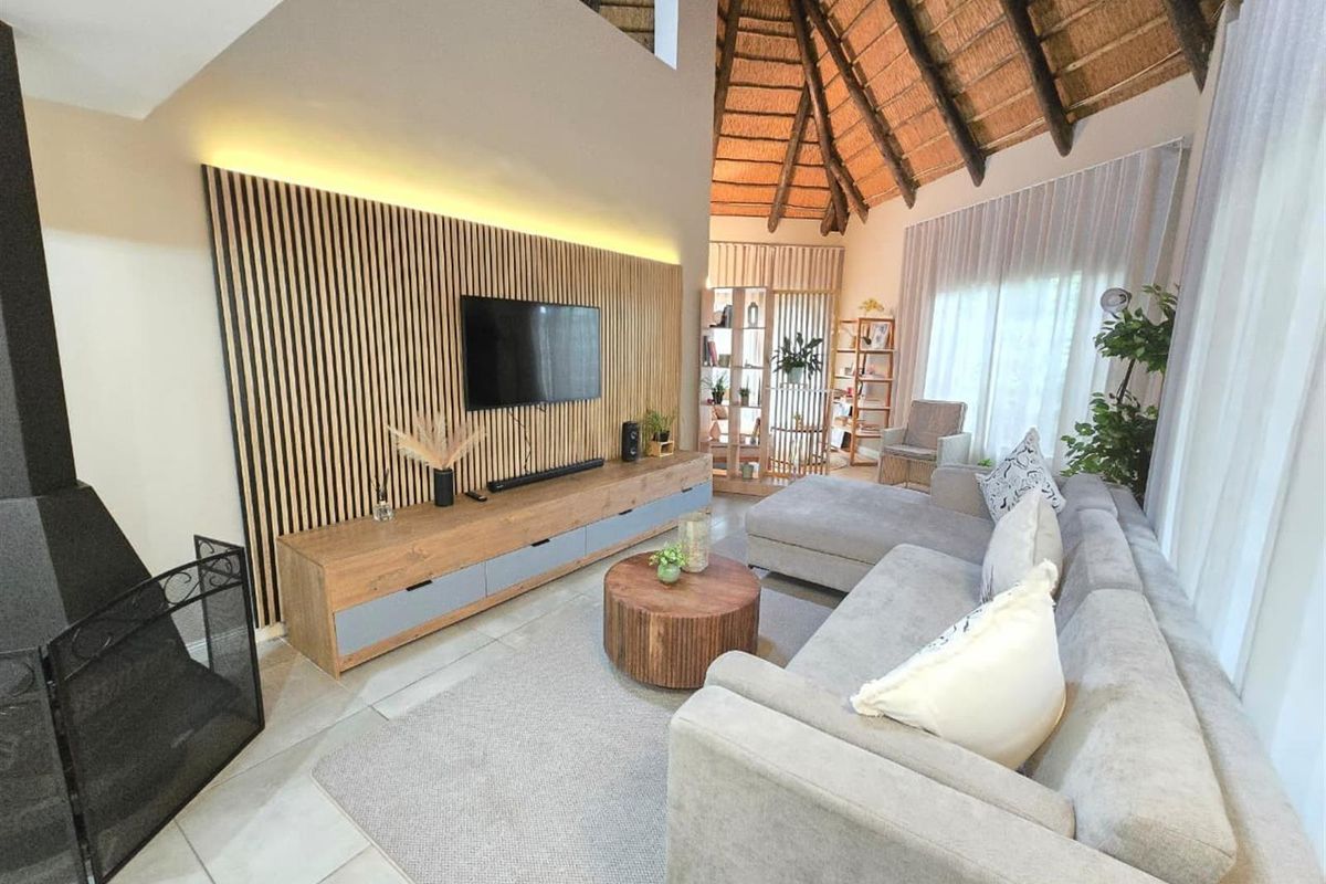 Spacious living room featuring a high vaulted thatched ceiling, modern timber slat feature wall with integrated lighting, and large windows providing natural light.