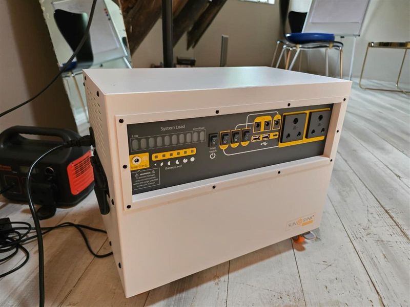 A portable Sunsynk solar power inverter unit featuring multiple power outlets, USB ports, and system load indicators, suitable for backup power solutions.