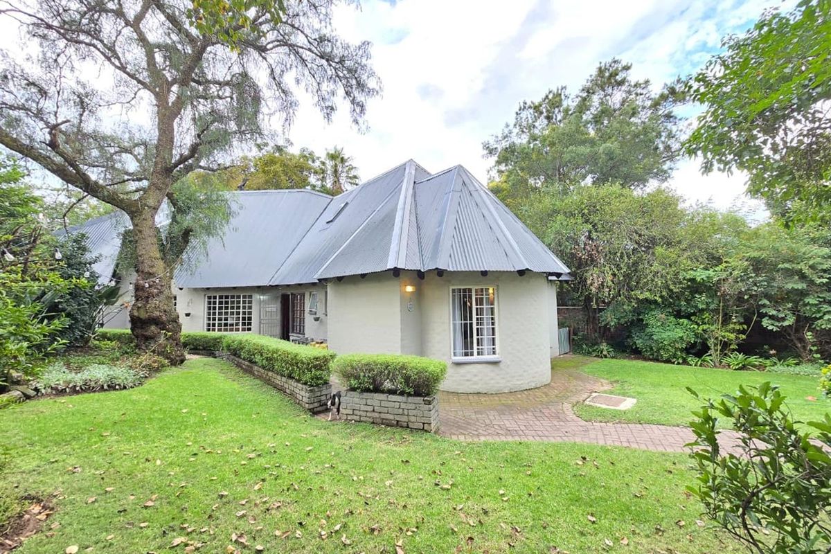 A view of the rear exterior of the house, featuring a curved wall design, corrugated metal roof, and a paved walkway through the garden.