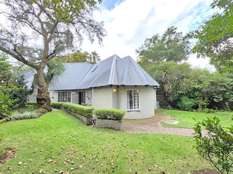 A view of the rear exterior of the house, featuring a curved wall design, corrugated metal roof, and a paved walkway through the garden.
