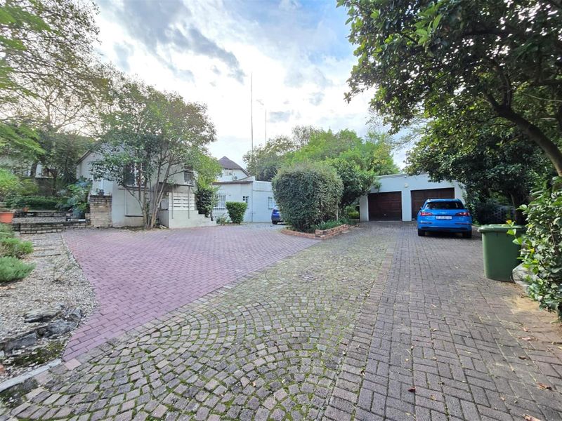 Front exterior view of the property featuring a paved driveway, double garage, and established garden surroundings.