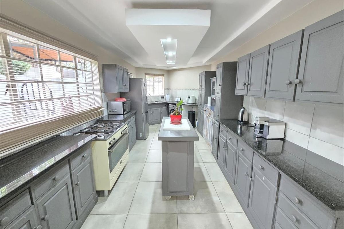 A galley-style kitchen featuring grey cabinetry, dark granite countertops, a central island, and a built-in gas stove with an integrated extractor fan.