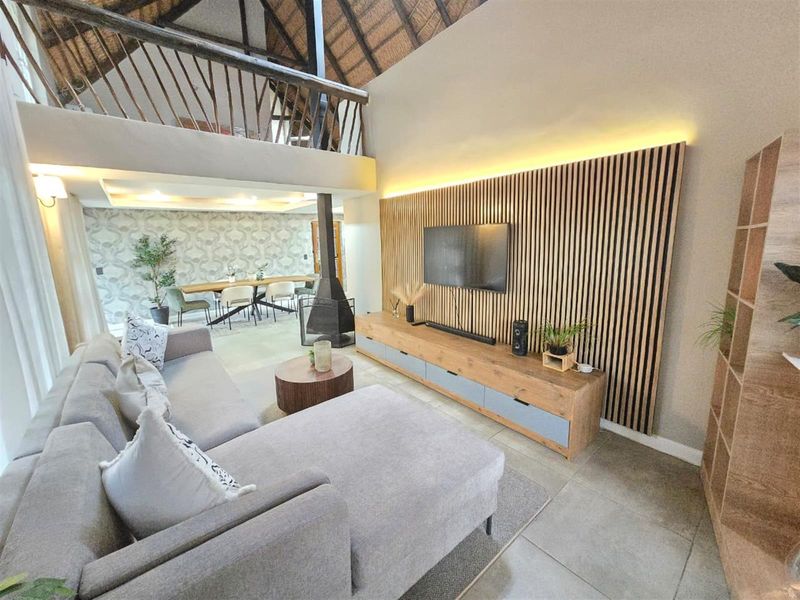 Spacious open-plan living area featuring a double-volume thatched ceiling, a modern slatted wood feature wall with integrated lighting, and a contemporary freestanding fireplace.