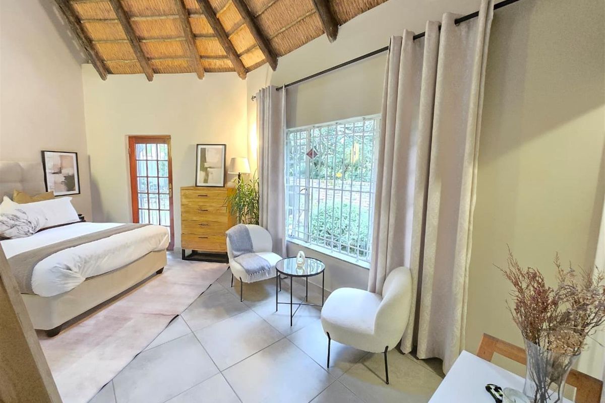 Spacious bedroom featuring a high vaulted thatched ceiling, tiled flooring, and large windows with security bars, offering a bright and airy atmosphere.
