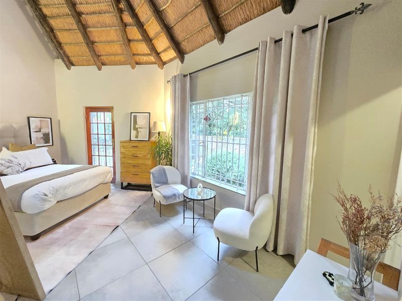 Spacious bedroom featuring a high vaulted thatched ceiling, tiled flooring, and large windows with security bars, offering a bright and airy atmosphere.