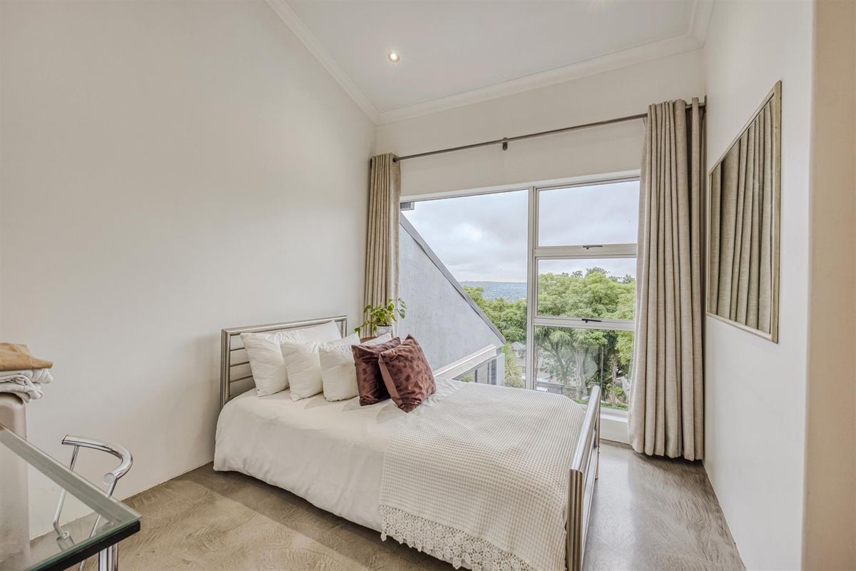 A bright bedroom featuring high vaulted ceilings, polished concrete flooring, and large windows offering scenic views.