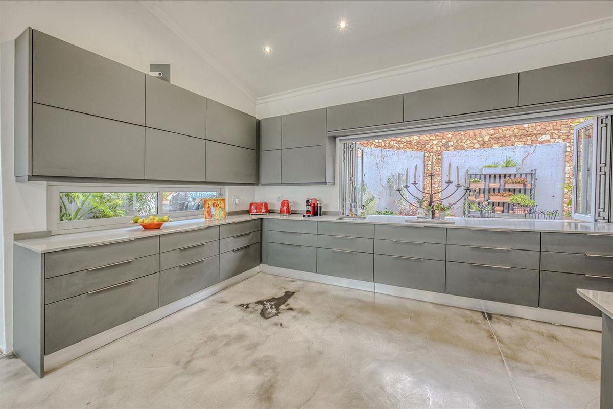 Modern kitchen featuring sleek grey cabinetry, stone countertops, and a large folding window opening to an outdoor courtyard area.