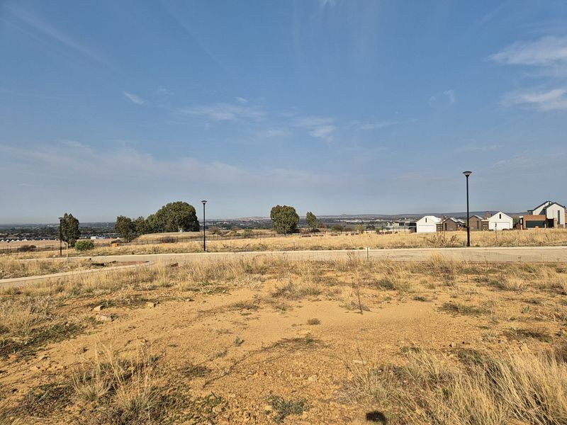 A view of the vacant residential land showing the surrounding landscape, paved road, and street lighting infrastructure.