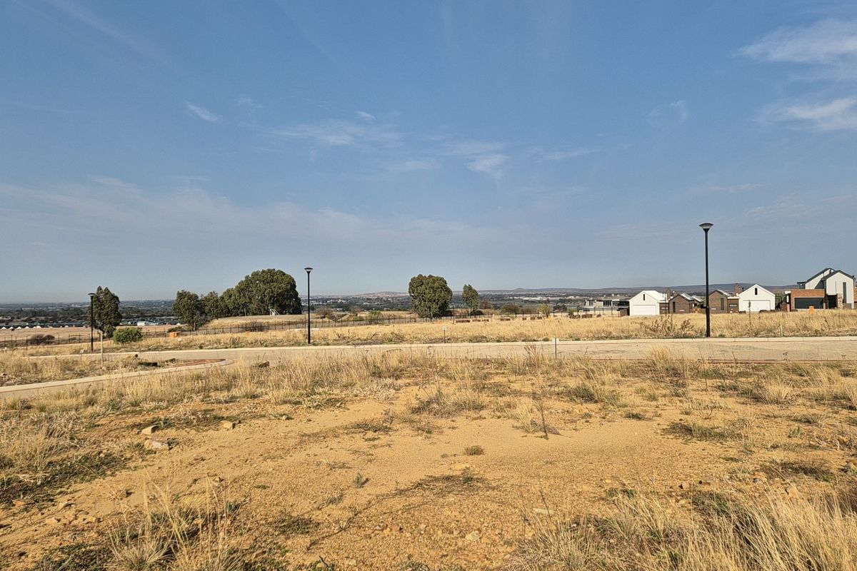 A view of the vacant residential land showing the surrounding landscape, paved road, and street lighting infrastructure.