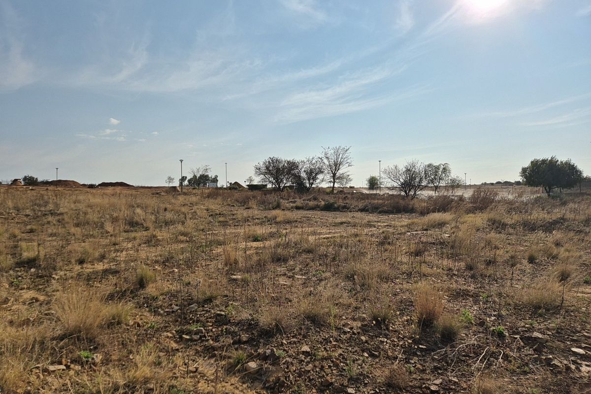 A wide-angle view of a vacant residential plot featuring natural dry vegetation and open terrain under a clear sky.
