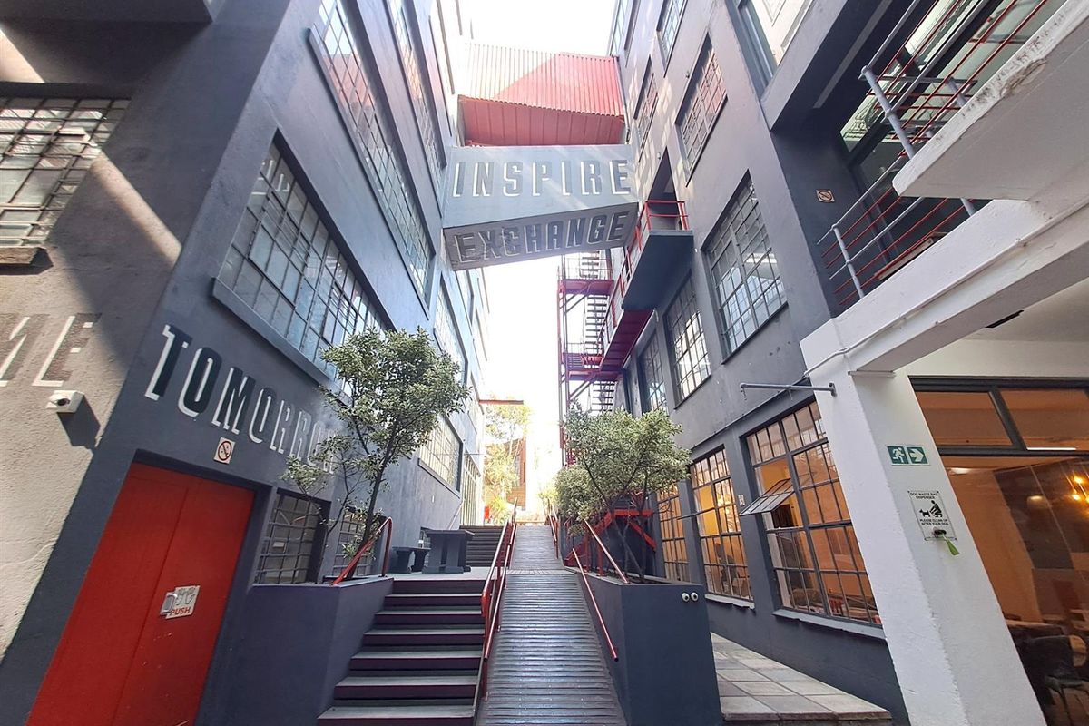 A modern industrial-style office complex courtyard featuring a connecting bridge, steel staircases, and multi-level building facades with large industrial windows.