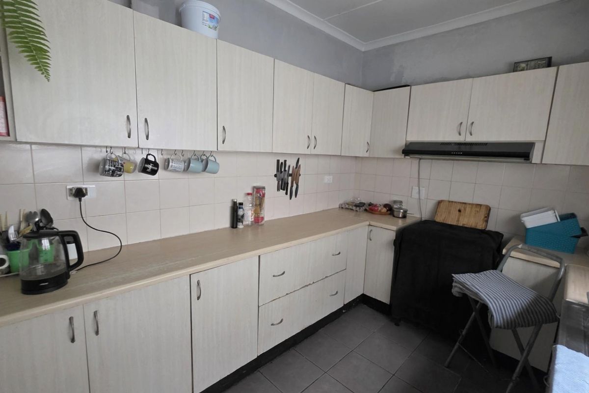A functional kitchen featuring light-toned cabinetry, tiled splashbacks, and a built-in extractor fan, offering ample storage and workspace.