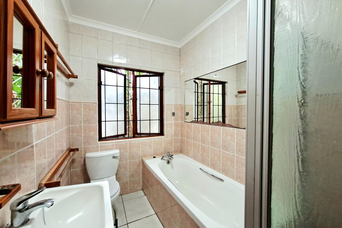 A functional bathroom featuring a bathtub, toilet, and vanity basin with tiled walls and a window providing natural light.