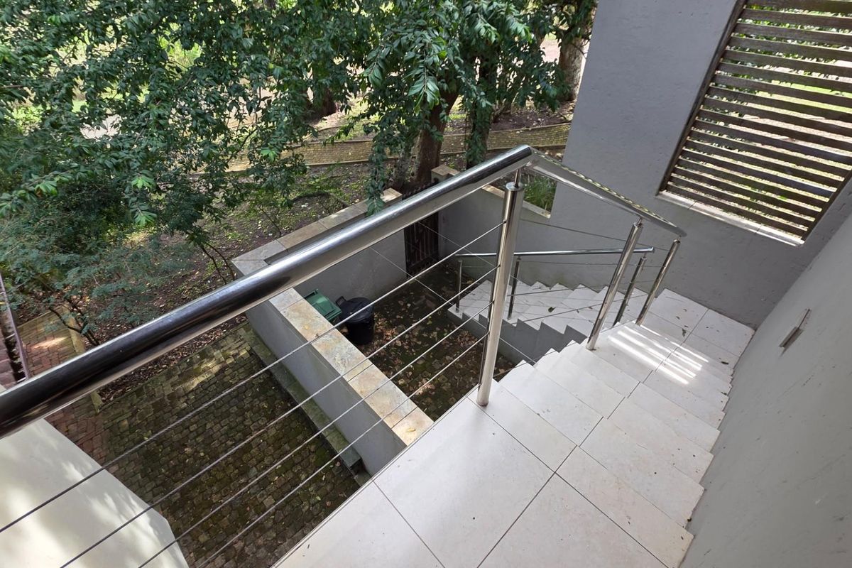 An outdoor staircase featuring modern tiled steps and a stainless steel balustrade with cable railings, overlooking a landscaped garden area.