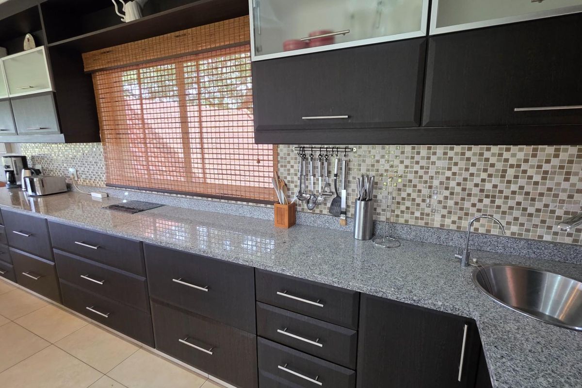 A well-maintained kitchen featuring dark wood cabinetry, granite countertops, a mosaic tile backsplash, and a stainless steel sink.
