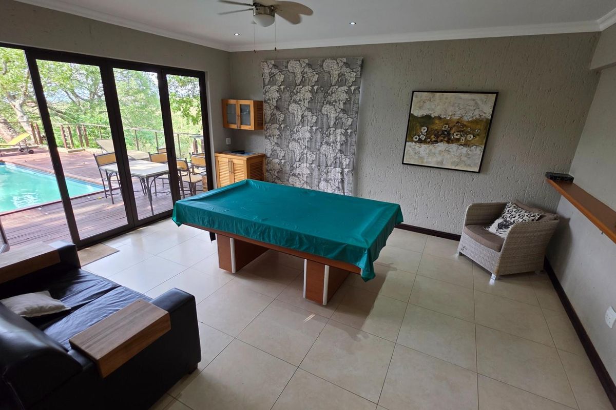 Spacious living area featuring large sliding glass doors opening onto a wooden deck with a swimming pool, tiled flooring, and recessed ceiling lighting.