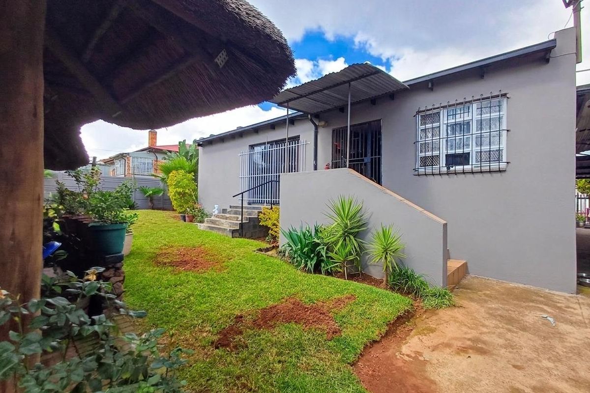 Rear exterior view of the house featuring a lawn, concrete steps, security bars on windows, and a thatched lapa structure.