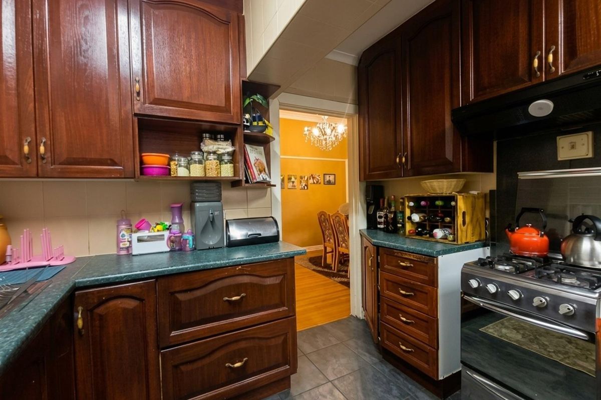 A functional kitchen featuring dark wood cabinetry, laminate countertops, and a gas stove with an extractor fan, leading into an adjacent dining area.