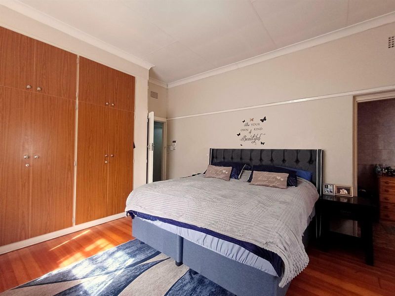 A well-maintained bedroom featuring polished hardwood flooring, classic picture rails, and extensive built-in wooden wardrobe storage.
